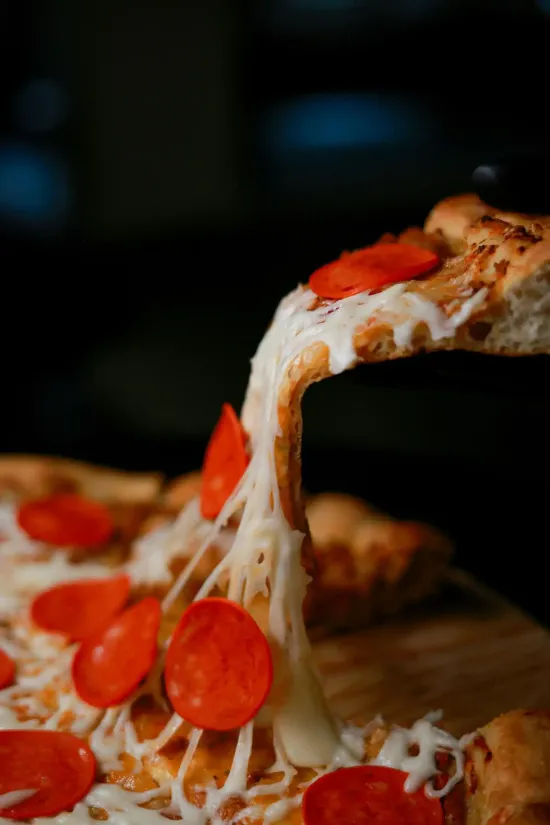 A slice of pepperoni pizza being lifted, with strings of melted cheese stretching