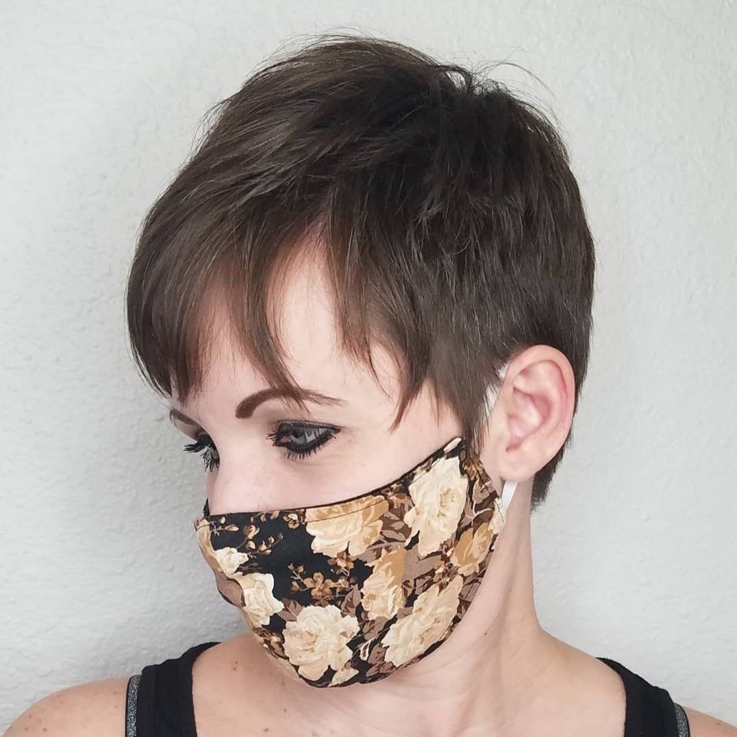 Person with short dark hair wearing a beige-and-black patterned face mask, looking down.