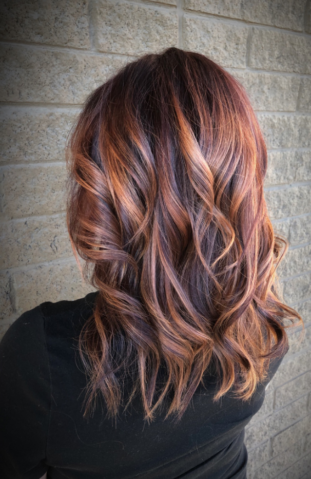 Wavy shoulder-length auburn hair with copper highlights against a gray brick wall