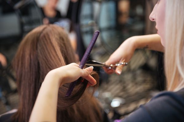 Hairdresser cutting long brown hair with scissors while holding a purple comb in a salon