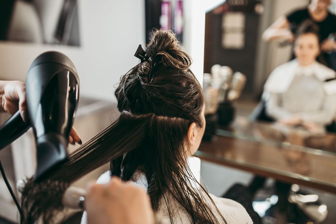Hair stylist blow-drying a client’s hair in a salon mirror station