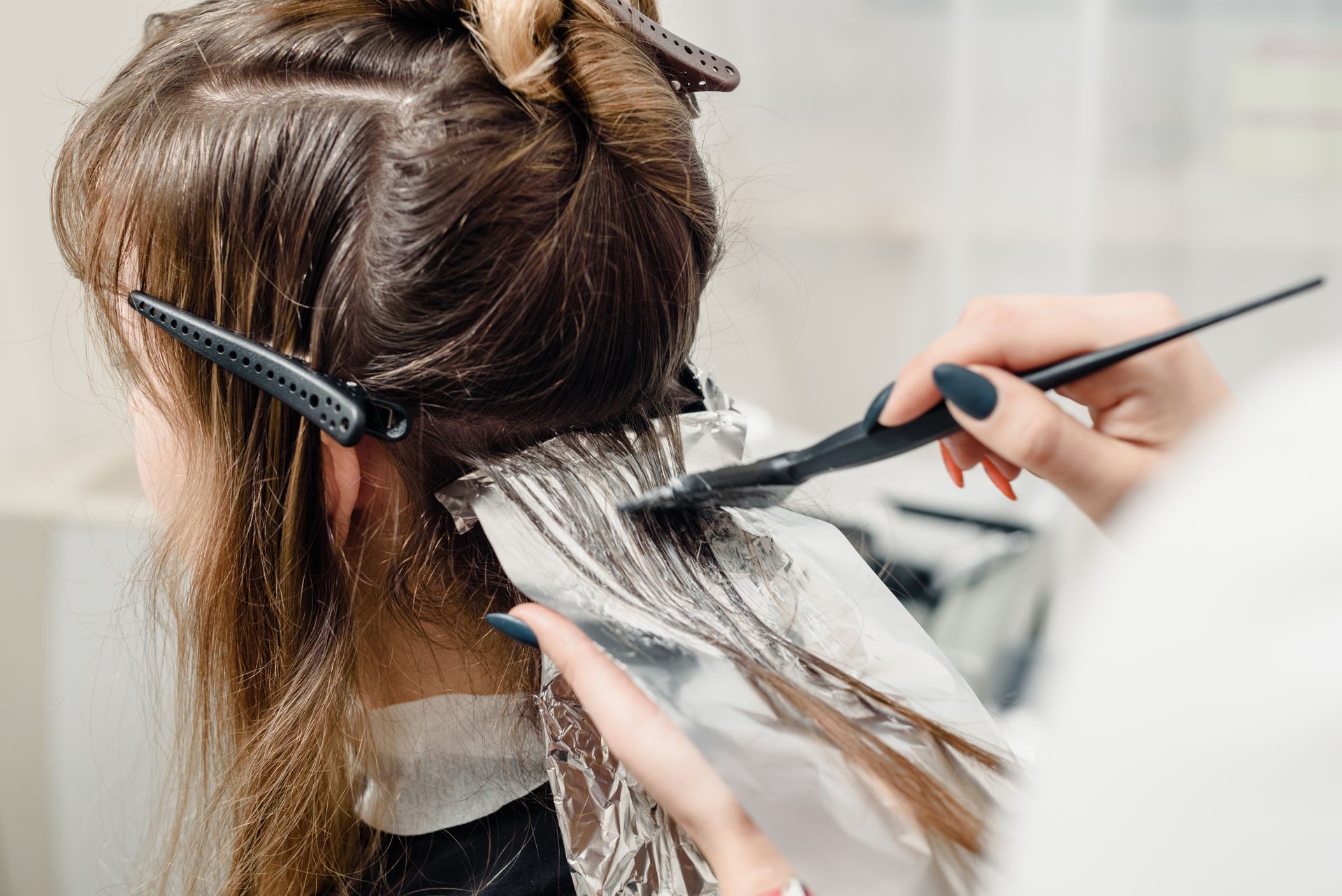 Hairdresser applying foil highlights to a client's brown hair in a salon