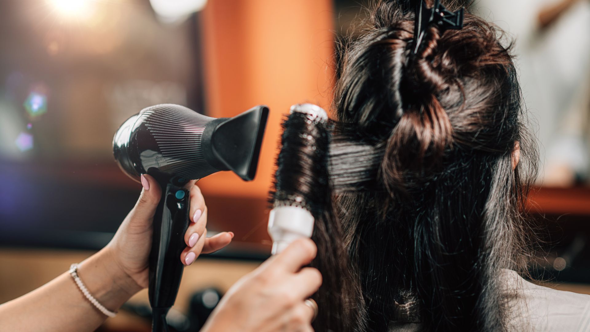 Hairdresser blow-drying and styling a customer’s dark hair in a salon