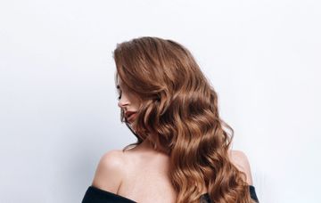 Woman with long wavy brown hair shown from behind against a light background