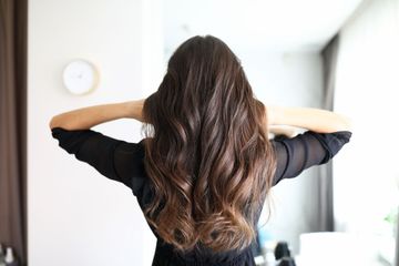 Person seen from behind adjusting long wavy brown hair in a bright room