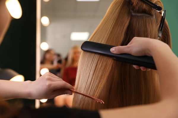 Hairdresser straightening long brown hair with a flat iron in a salon