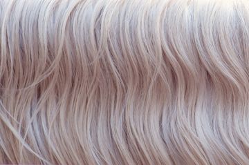 Close-up of wavy platinum blonde hair with soft pink-tinted highlights.