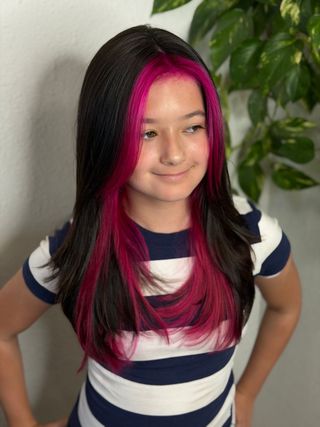 Person wearing a black-and-pink wig and striped shirt, standing indoors with hands on hips.