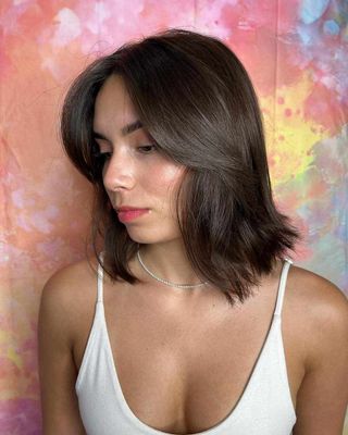 Woman with dark shoulder-length hair in a white tank top against a colorful pastel backdrop