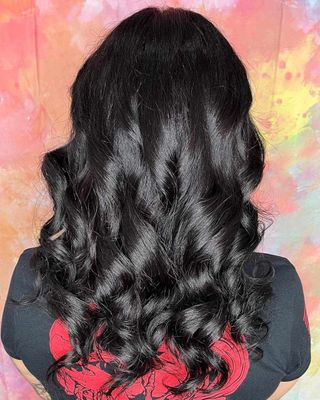 Back view of long, wavy black hair against a pink and yellow abstract background