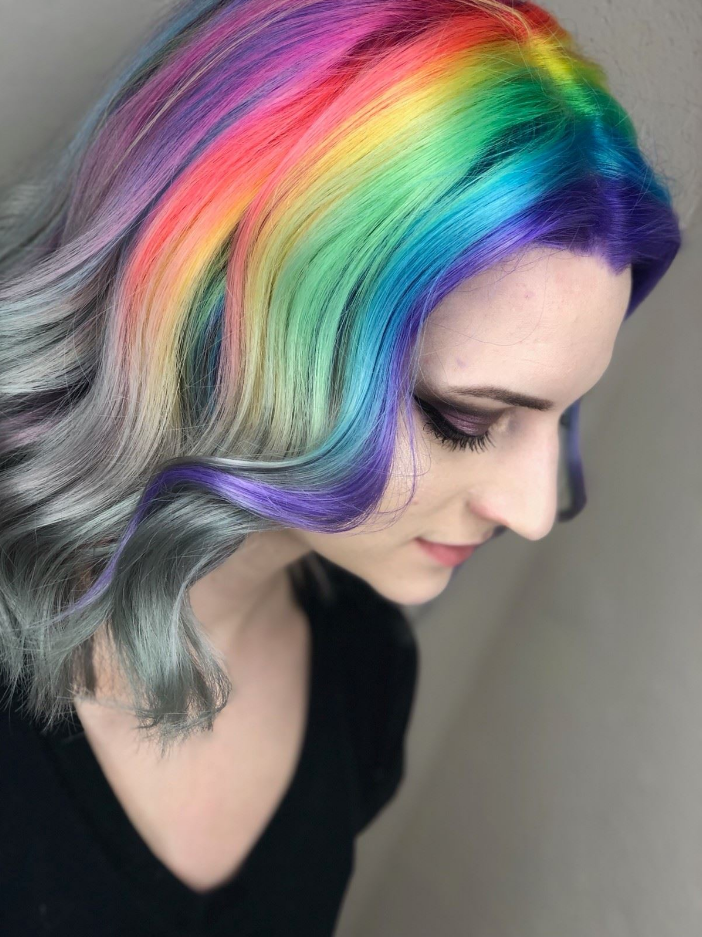 Profile of a woman with vibrant rainbow hair and a gray underlayer, looking downward against a plain background