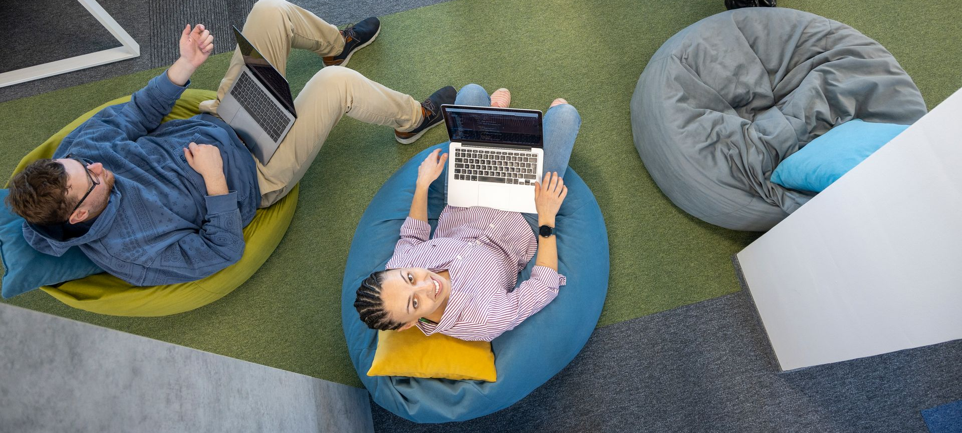 Three people using laptops while relaxing on beanbag chairs in an office.