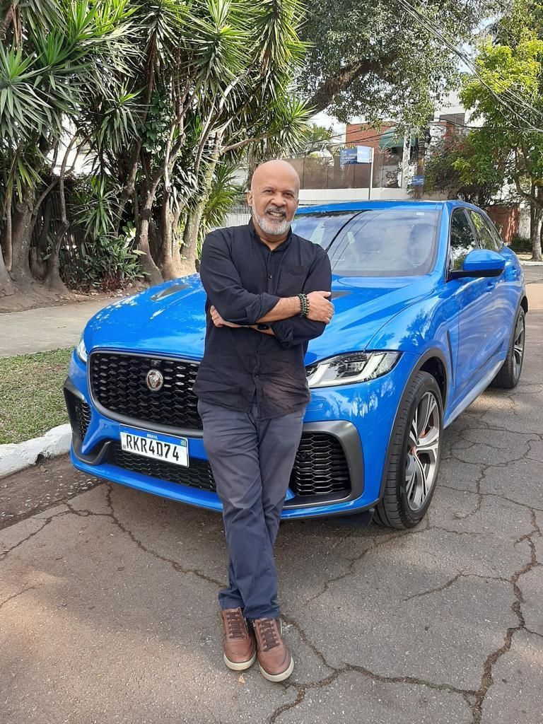Um homem com barba está parado na frente de um carro azul.