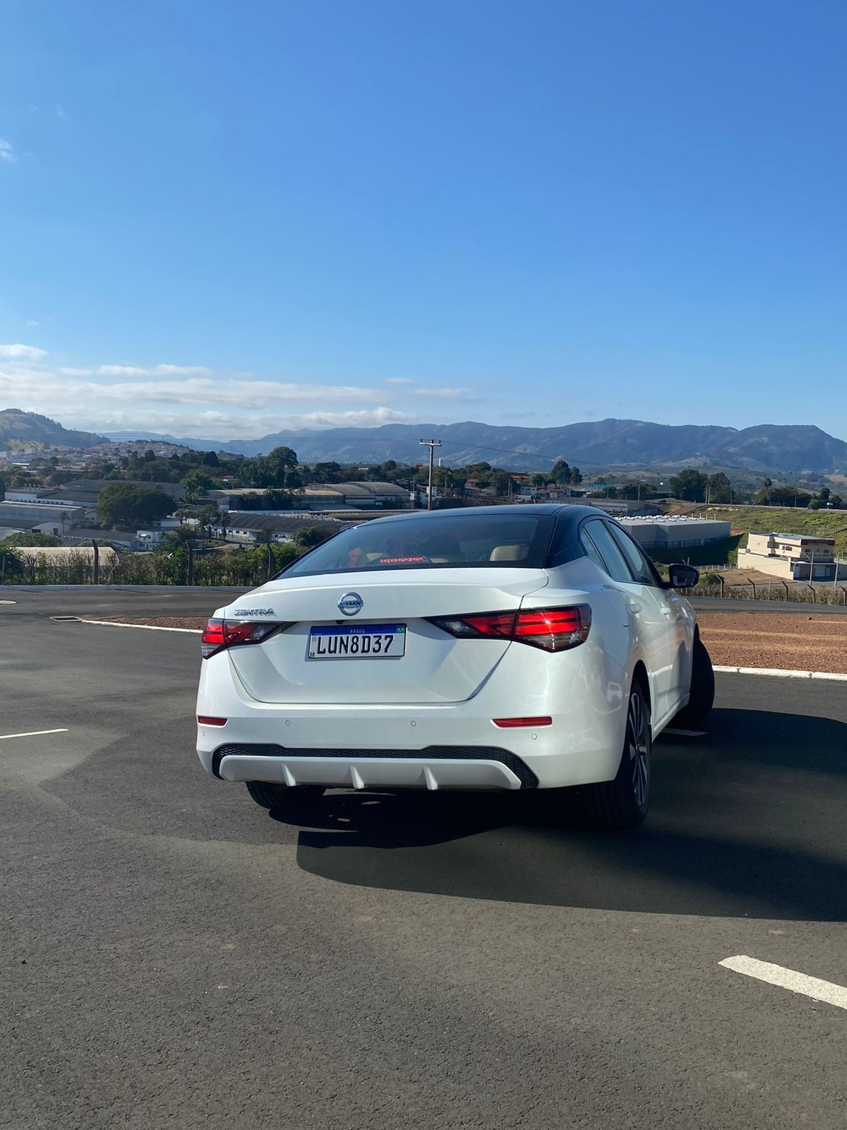 Um carro branco está dirigindo por uma estrada com montanhas ao fundo.