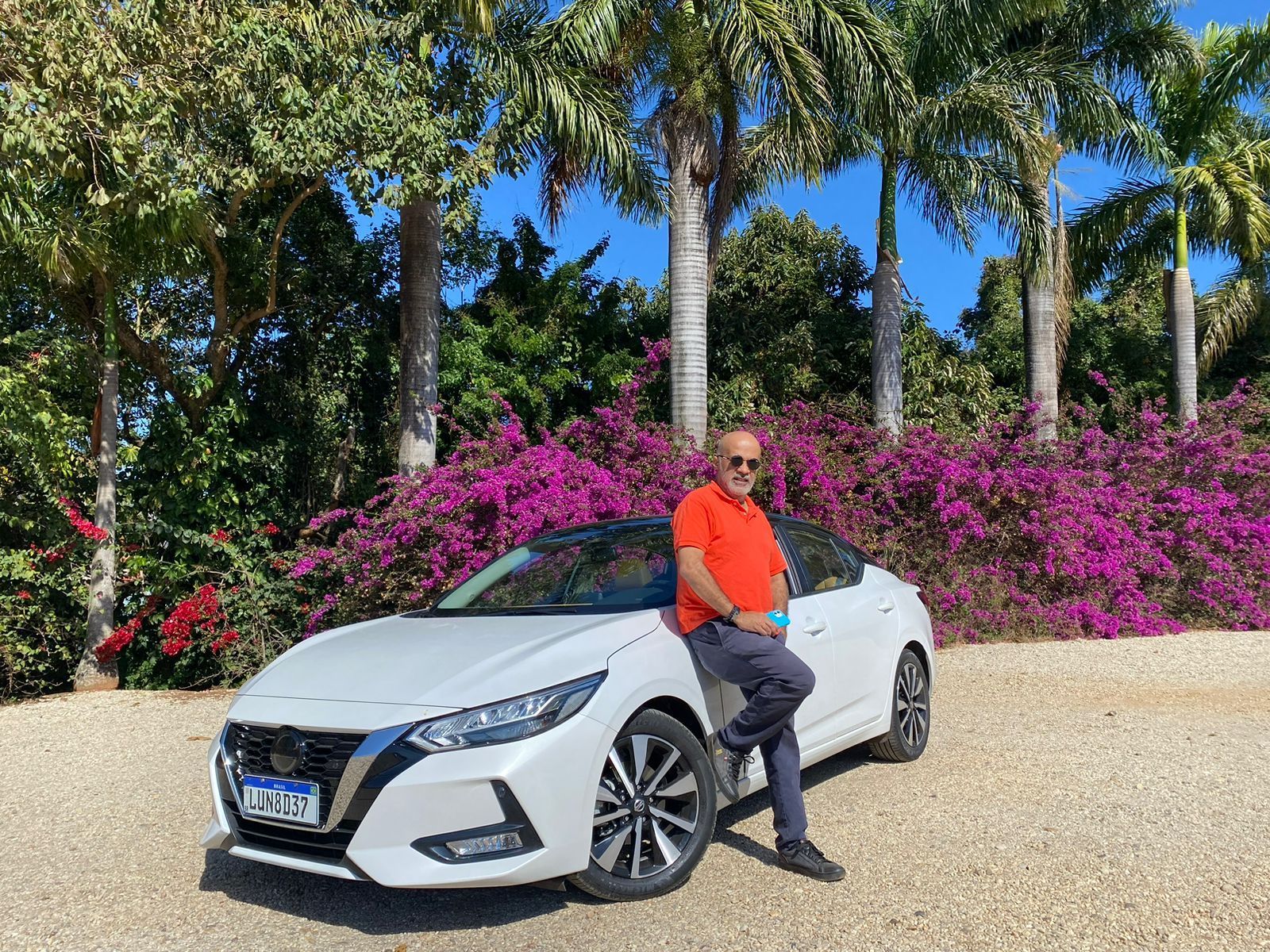 Um homem está sentado no capô de um carro branco.