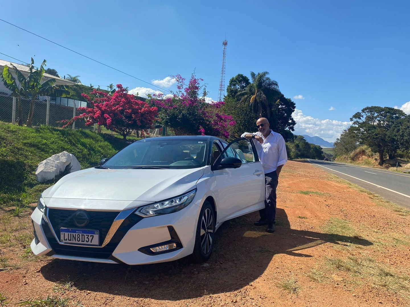 Um homem está parado ao lado de um carro branco na beira da estrada.