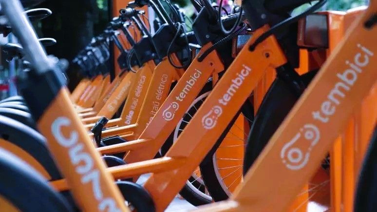Uma fileira de bicicletas laranjas estão estacionadas uma ao lado da outra
