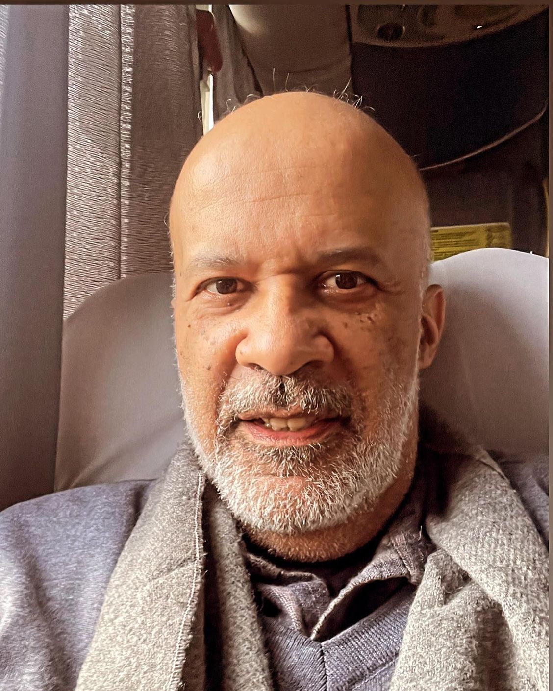 Um homem careca com barba está sentado em uma cadeira.