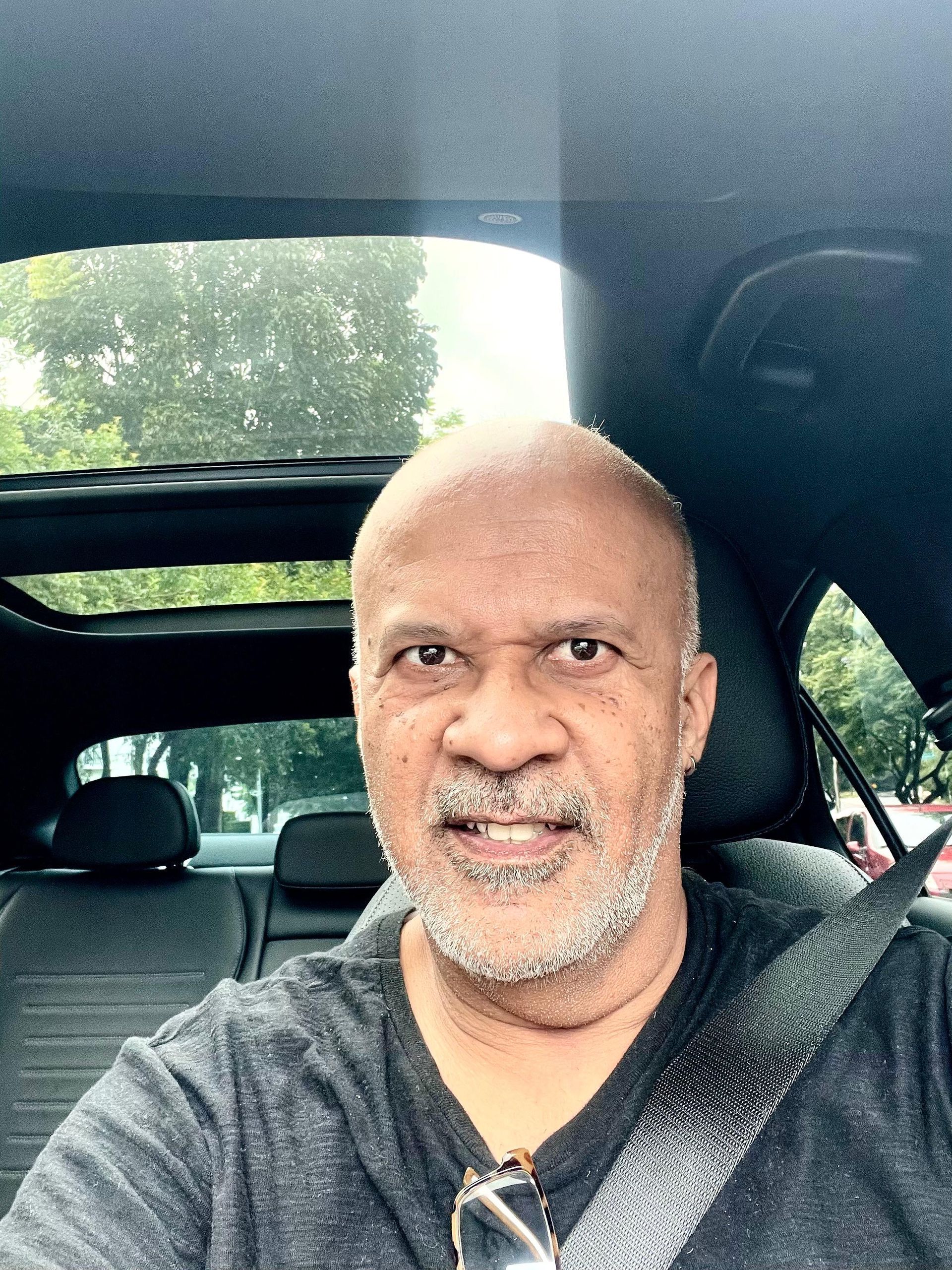 Um homem com barba está sentado no banco de trás de um carro.