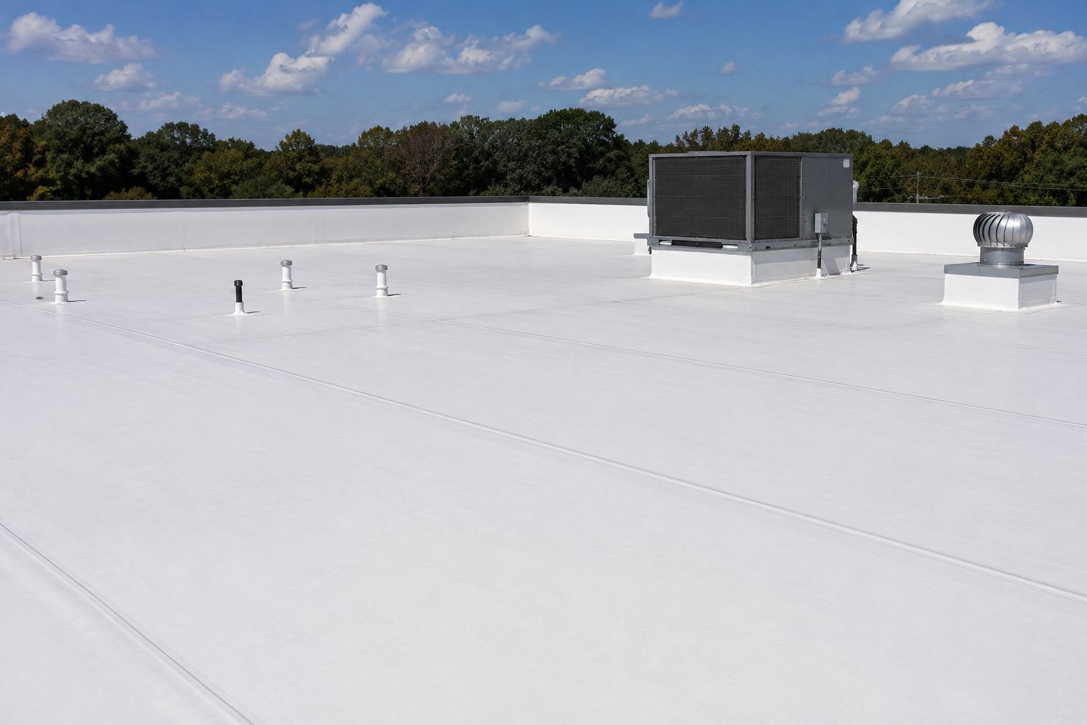 White flat rooftop with HVAC units under a blue sky, bordered by trees.