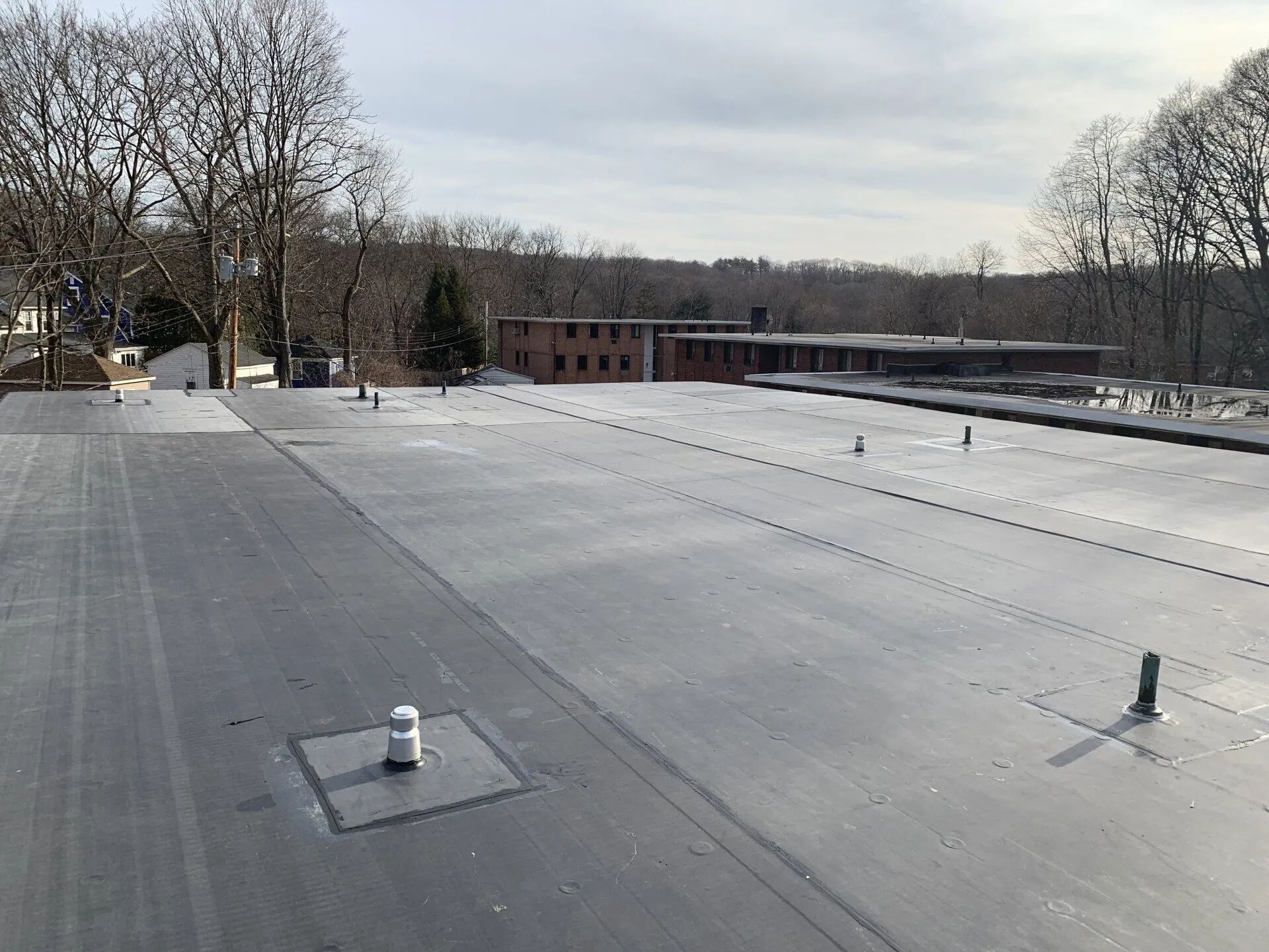 Flat rooftop with vents, trees in the distance, and a cloudy sky beyond a brick building.