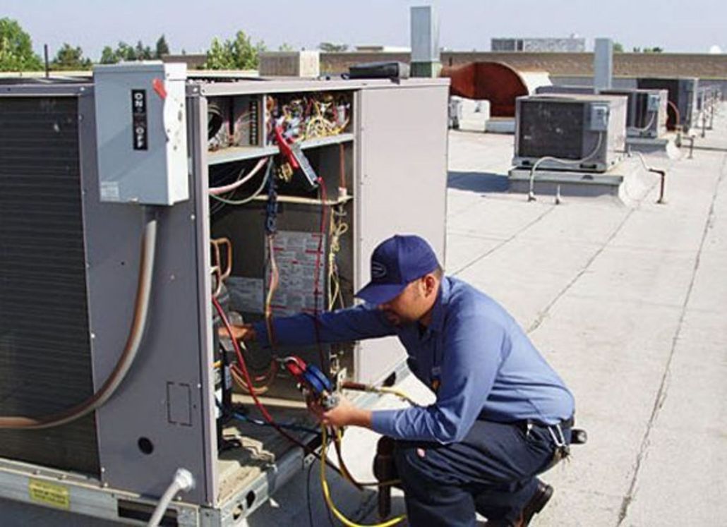 A man is working on an air conditioner on the roof of a building