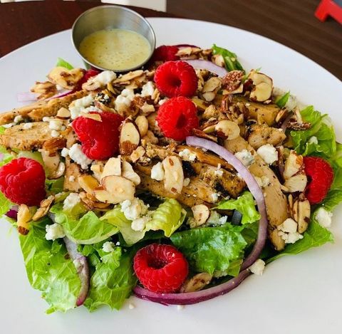 Salad with lettuce, raspberries, sliced almonds, red onion, and dressing on a white plate
