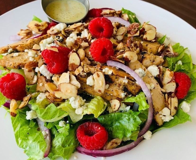 Salad with lettuce, chicken, red onion, raspberries, almonds, and dressing on a white plate