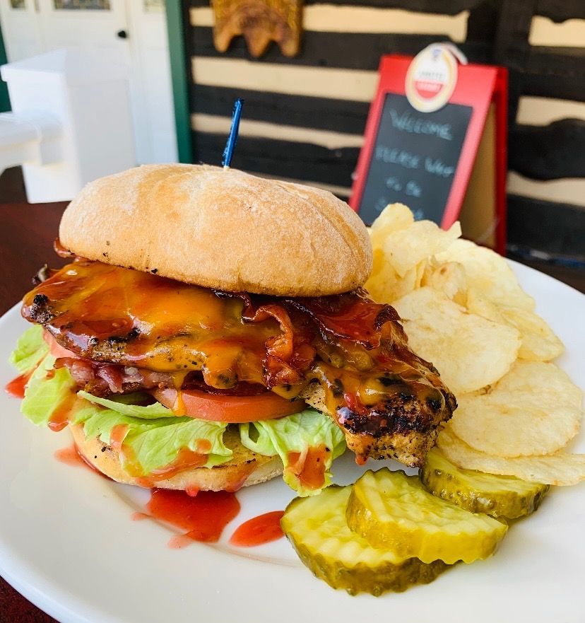 Grilled cheeseburger with lettuce, tomato, pickles, and chips on a white plate at a cafe table