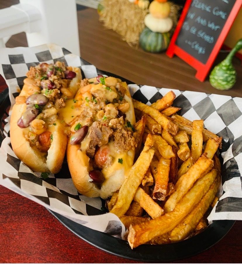 Two loaded hot dogs and seasoned fries in a black basket lined with checkered paper