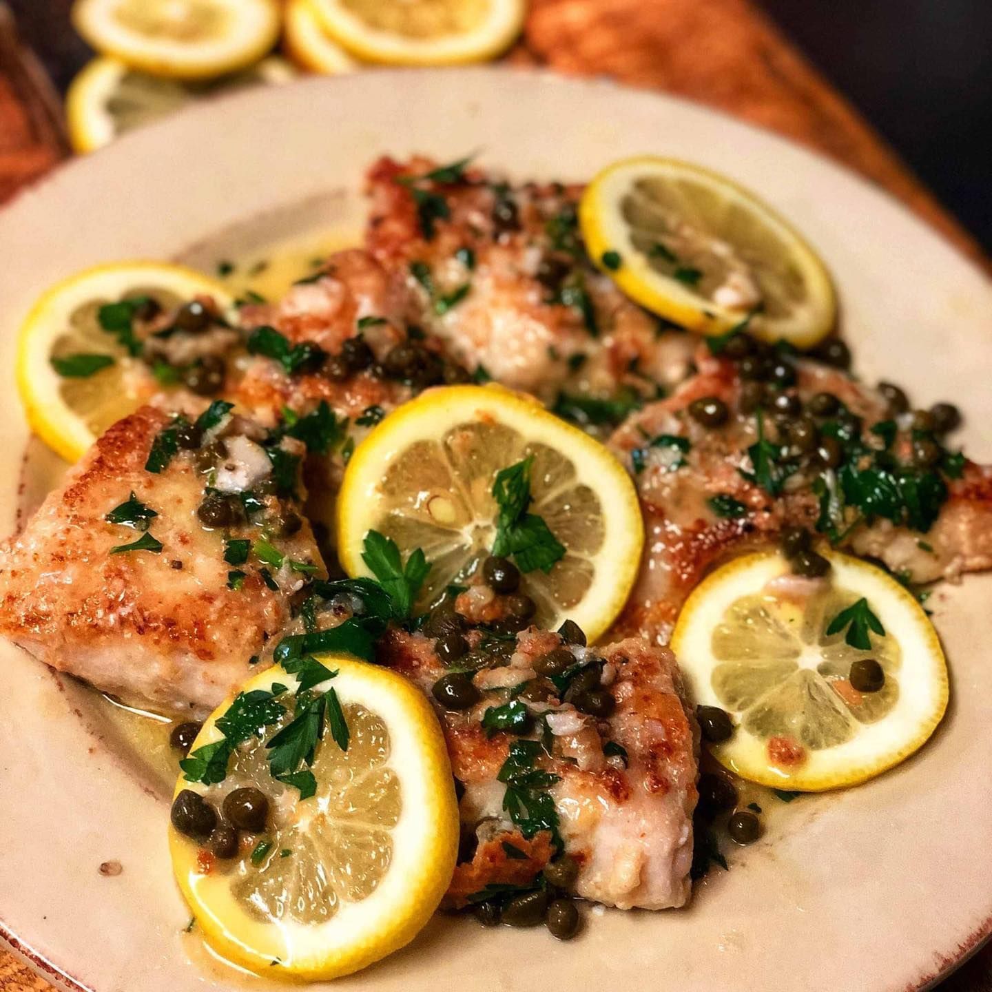 Seared fish fillets topped with lemon slices and capers on a white plate