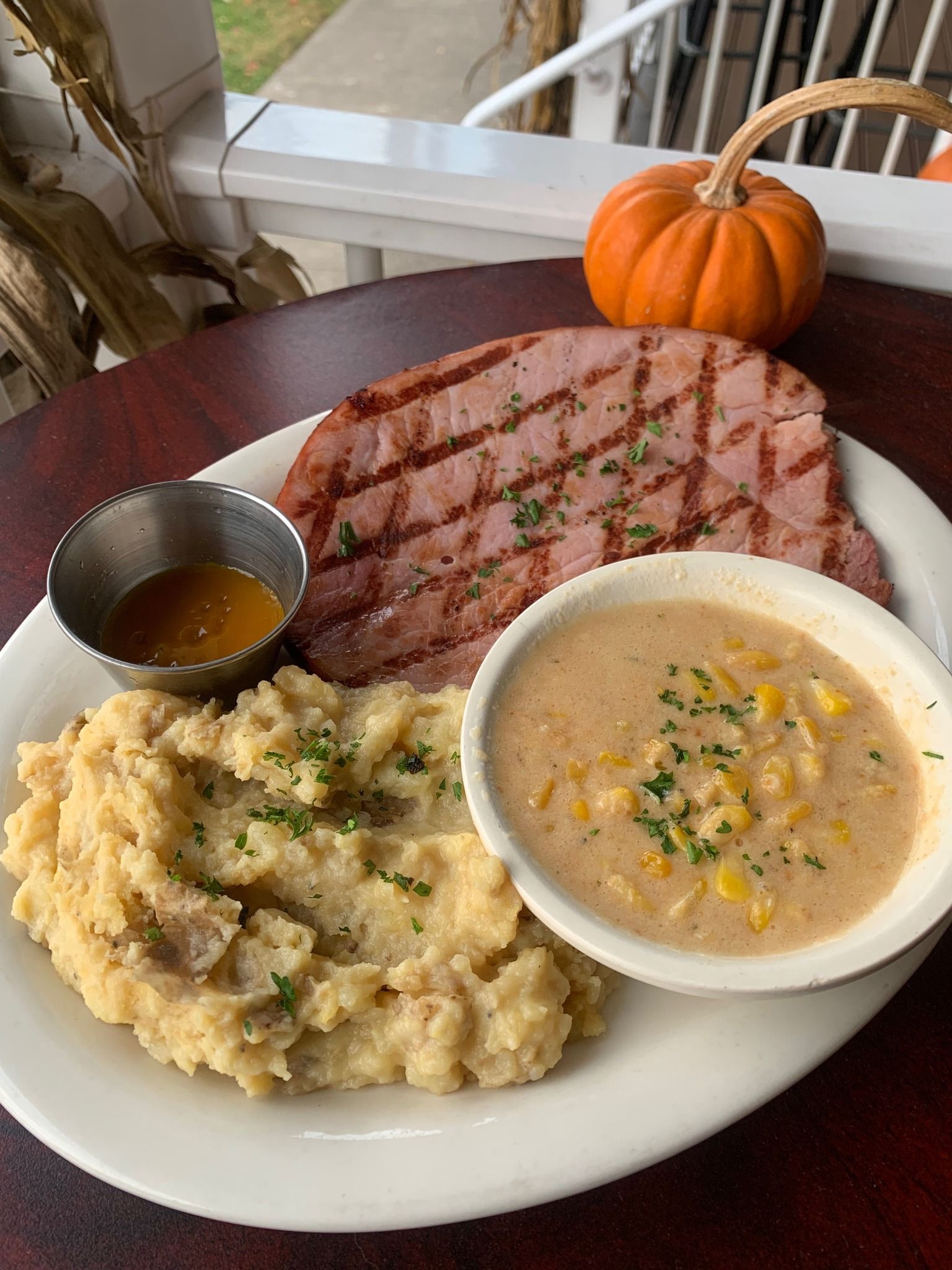 Plate of grilled steak with mashed potatoes, creamy soup, and sauce, with a small pumpkin on the table.