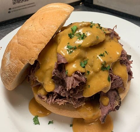 Pulled beef sandwich with melted cheese sauce on a white plate