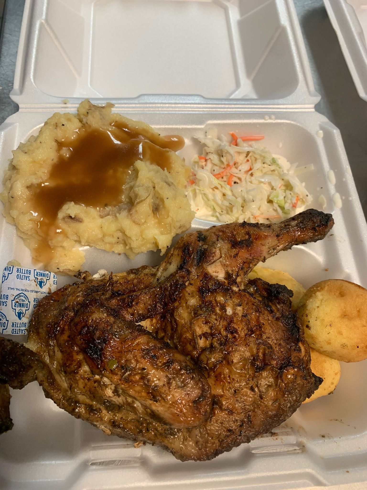 Takeout box with grilled chicken, mashed potatoes with gravy, coleslaw, and a dinner roll