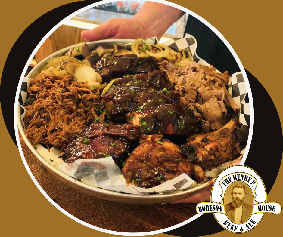 Tray of barbecue meats and sides on checkered paper at a restaurant table with a logo sticker.