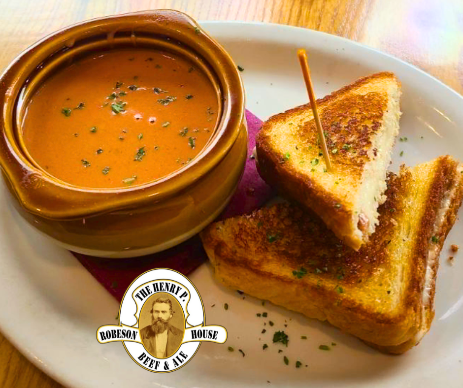 Creamy tomato soup in a bowl with grilled cheese sandwich halves on a white plate, garnished with herbs