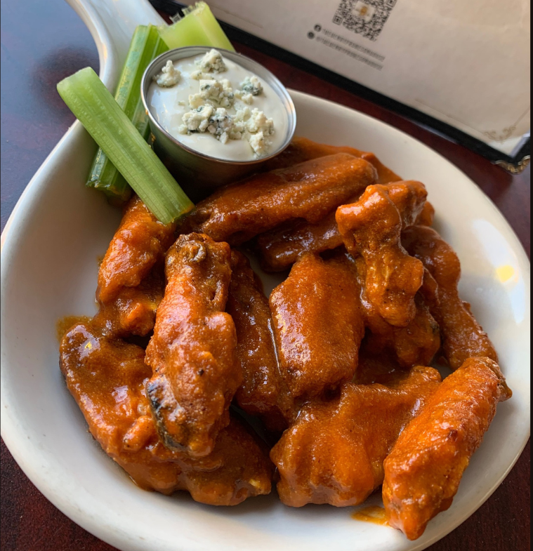 Plate of saucy buffalo chicken wings with celery sticks and a cup of blue cheese dressing