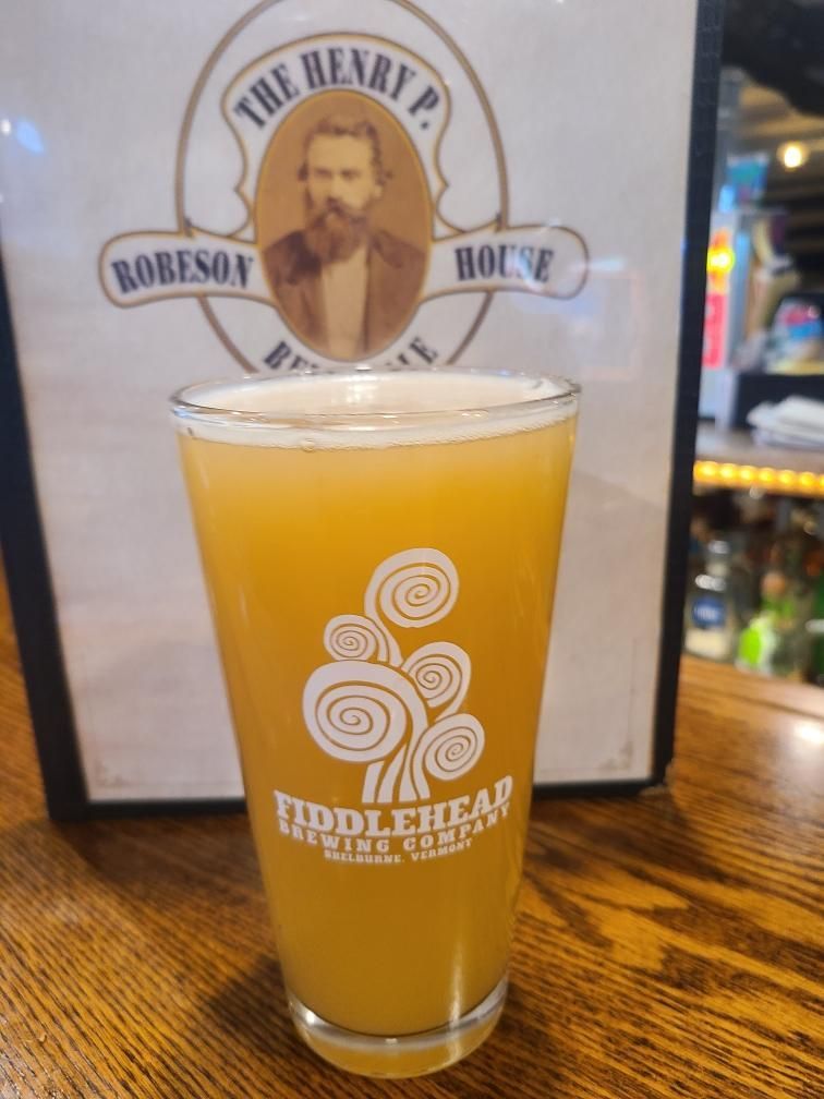 Pint of hazy orange beer on a bar, with The Henry sign blurred in the background