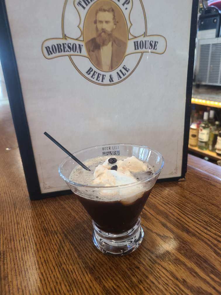 Glass of chocolate dessert topped with whipped cream and a spoon, on a wooden table in a restaurant.