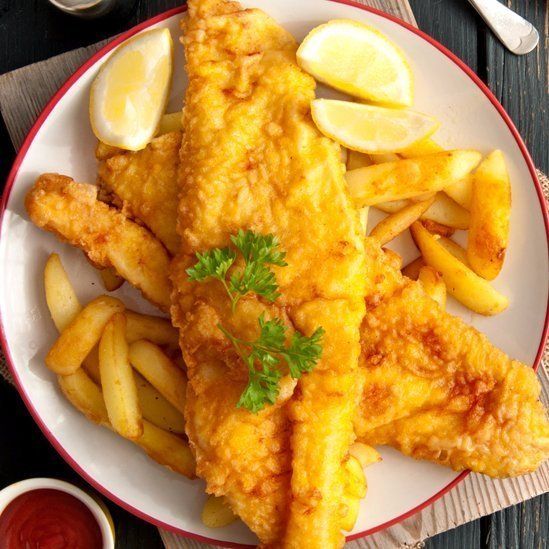 Plate of fish and chips with lemon wedges and parsley, served with ketchup on a dark table.