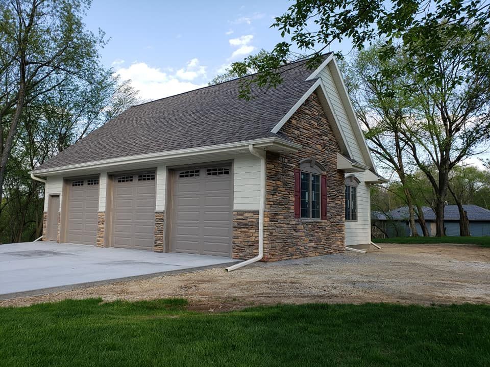 A garage with three garage doors is sitting in the middle of a lush green field.
