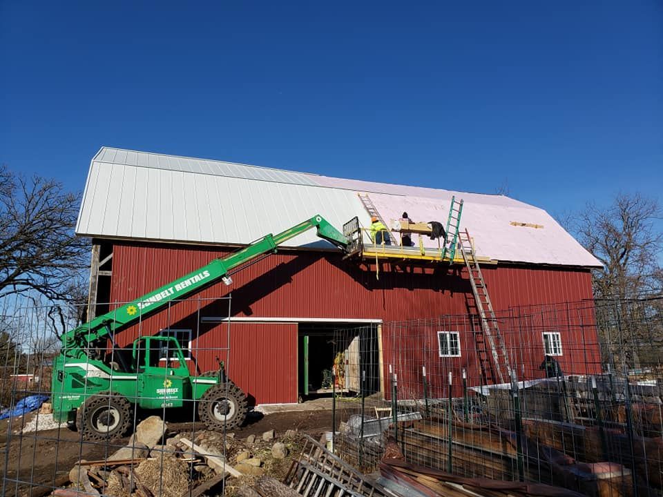 A green forklift is parked in front of a red barn.