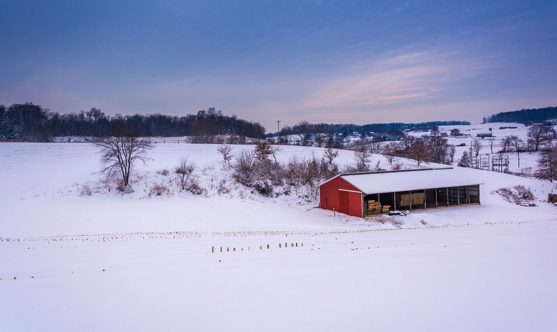 Red barn in a snowy field under a cloudy winter sky with trees in the background.