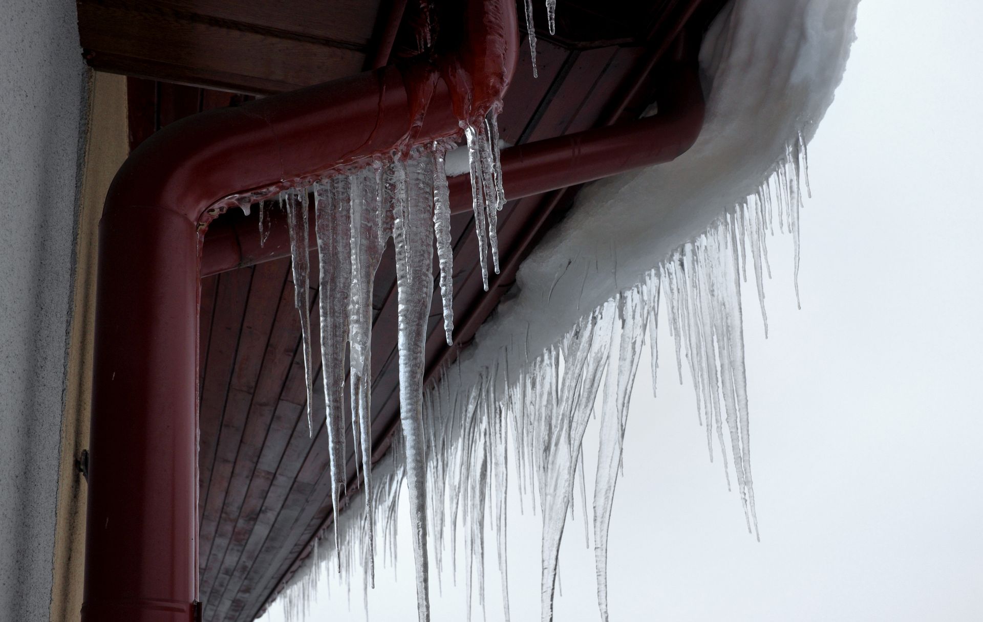 Icicles hanging from a red gutter on a building's edge.