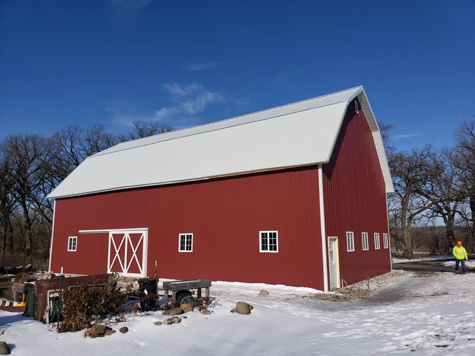 Red barn with a white roof, in a snowy field on a sunny day.