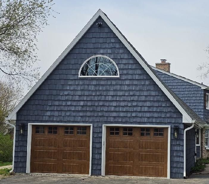 Front view of a custom two-car garage in Beloit, WI with wood doors, shake-style siding, and decorative gable window.