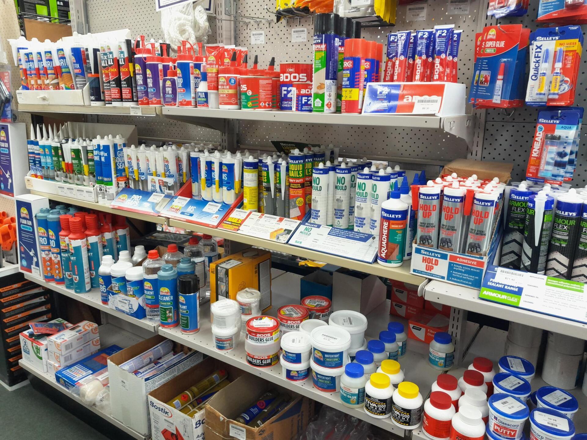Shelves in a hardware store stocked with various tubes of caulk, sealants, and adhesive bottles.