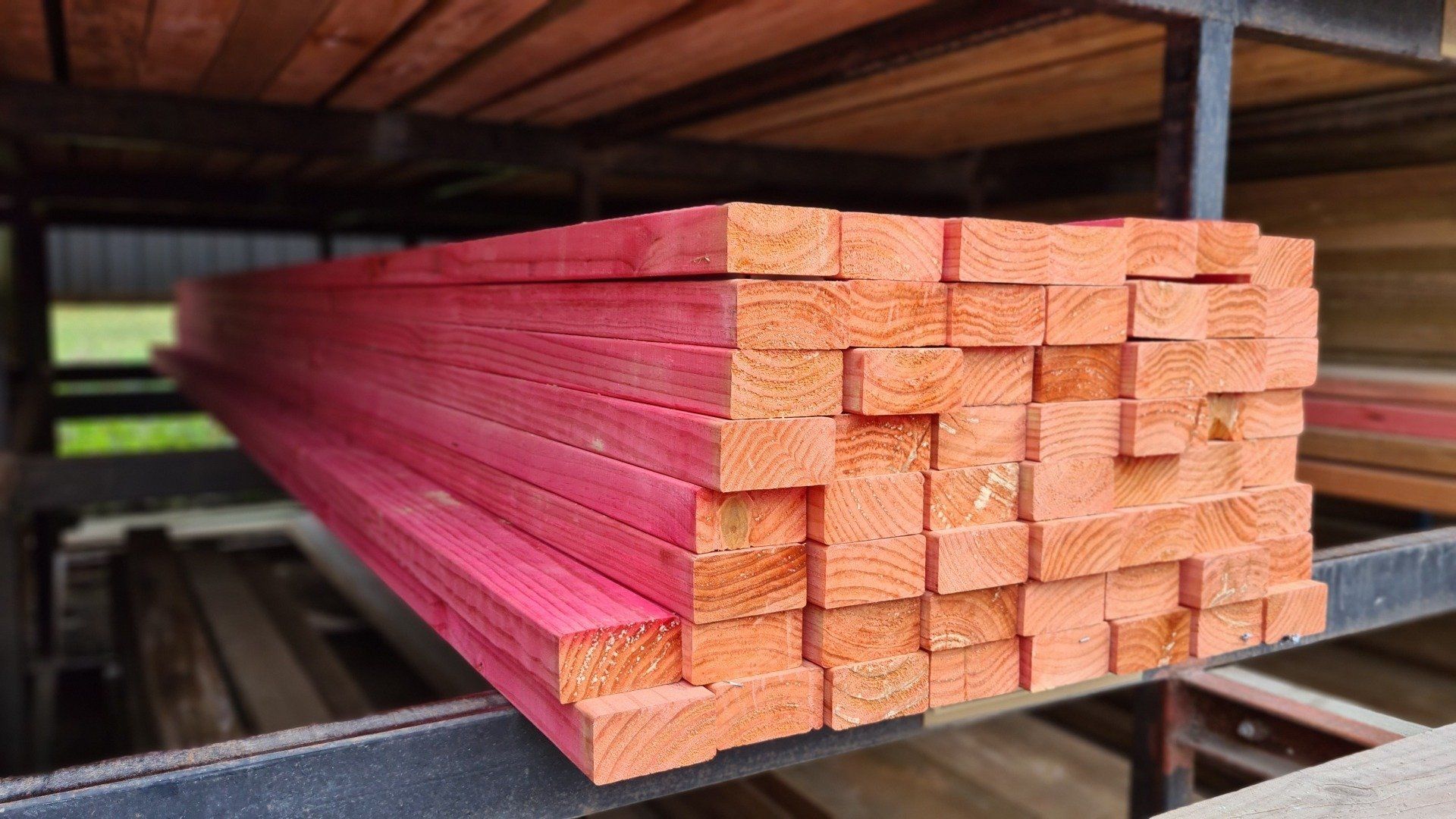 A stack of lumber boards with red-stained ends rests on a metal storage rack.