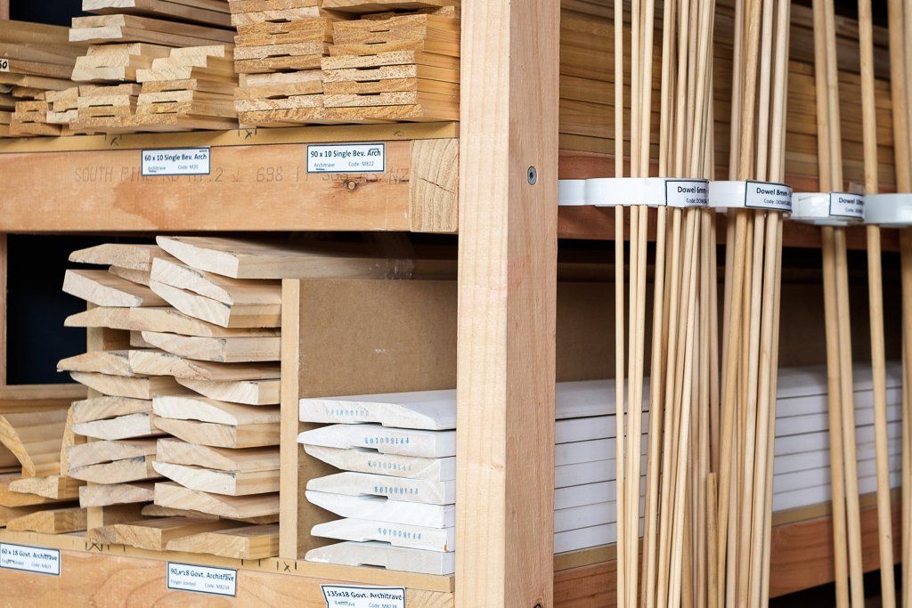 Wooden shelves in a hardware store stocked with various pieces of trimmed wood molding and long, thin dowels.