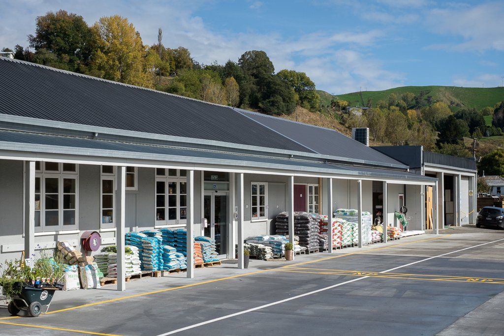 A single-story, grey warehouse-style building with a covered walkway displaying stacks of bagged products for sale.